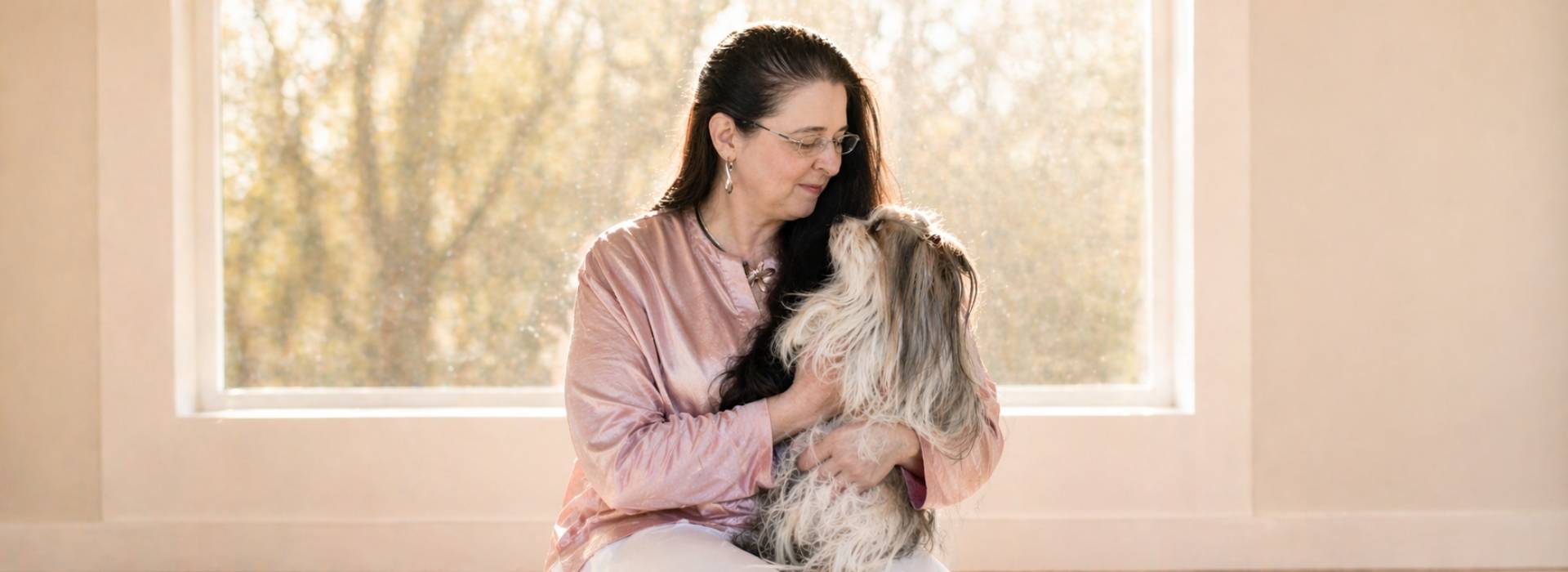 Frau sitzt in warmem Licht mit ihrem alten Hund und schaut ihn liebevoll an, ruhige Verbindung am Lebensende